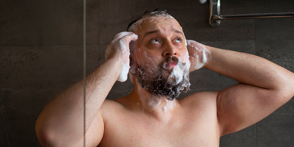 A man washing his beard in the shower.