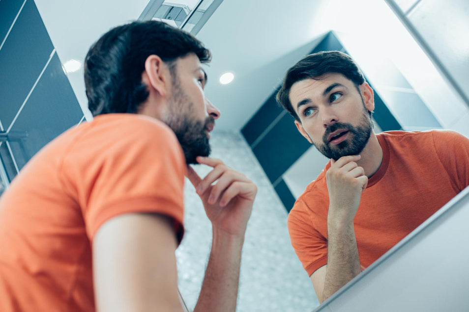 man looking at the mirror curious on how to make his beard healthier, fuller and more radiant looking.